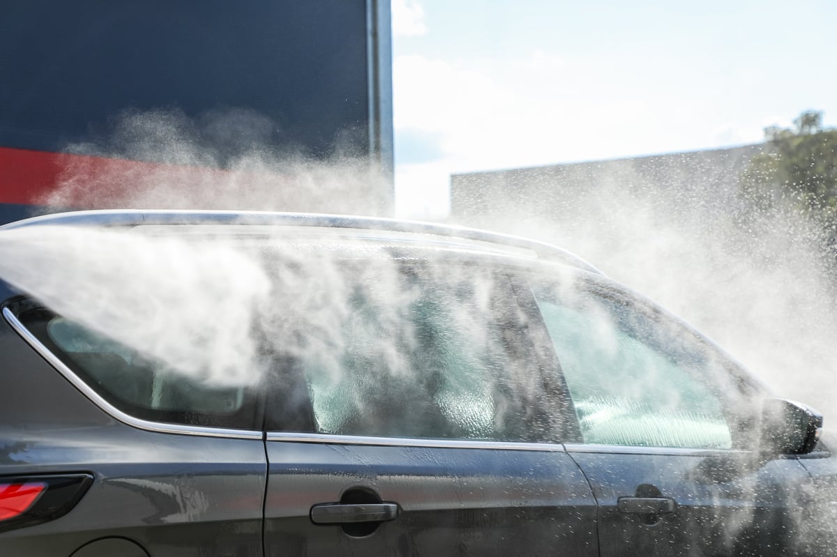 Car being rinsed with a high-pressure jet in bright sunlight